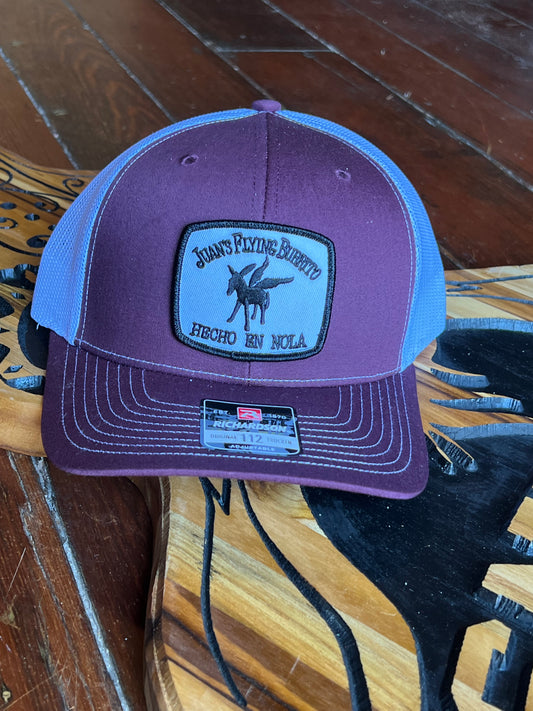 A picture of the Maroon two-tone trucker cap with embroidered "hecho" patch logo