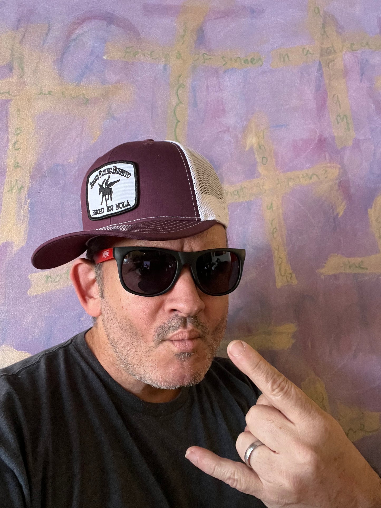 A picture of a total bro making rock&roll hand while wearing the two-tone maroon trucker cap with embroidered "hecho" patch logo
